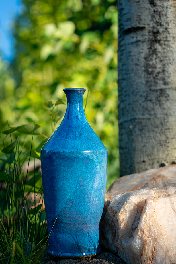 Azure blue white stoneware bottle vase by Converse Fields photographed outside in Steamboat Springs Colorado against rock, grass and Aspen tree