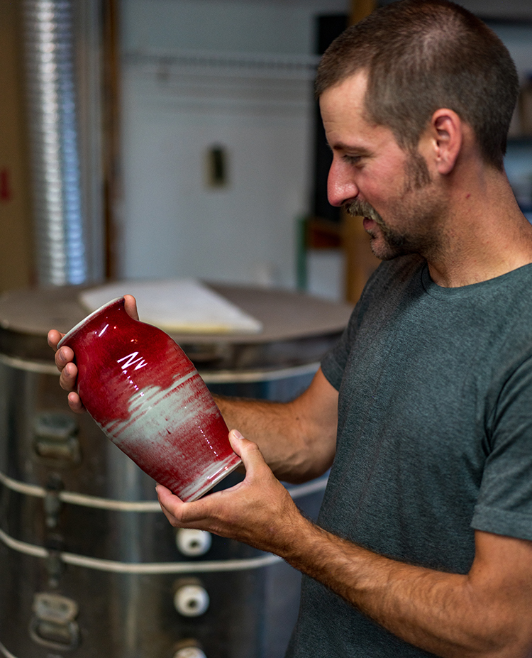 half body photo of potter Converse Fields inspecting copper red and celadon vase after firing